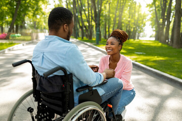 Cordial black lady holding her handicapped boyfriend's hand, expressing love at urban park