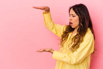 Young mexican woman isolated on pink background shocked and amazed holding a copy space between hands.