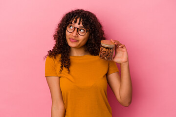 Young mixed race woman holding an almond jar isolated on pink background dreaming of achieving goals and purposes