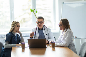 Doctors having a meeting seated at a table in front of a computer discussing case histories in...