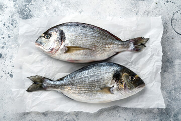 Raw dorado fresh fish or sea bream with ingredients for making lemon, thyme, garlic, cherry tomato and salt on light grey slate, stone or concrete background. Top view with copy space.