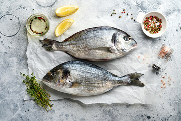 Raw dorado fresh fish or sea bream with ingredients for making lemon, thyme, garlic, cherry tomato and salt on light grey slate, stone or concrete background. Top view with copy space.