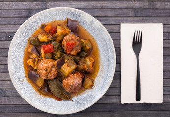 top view of plate of baked meatballs with stewed eggplant, zucchini, green peppers and tomatoes in bowl