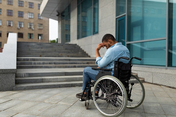 Upset handicapped black man in wheelchair in front of stairs without ramp, having no possibility to enter building