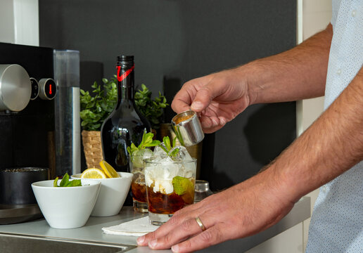 Young man making cocktail drinks in the kitchen at home. Homemade cocktail base on coffee rum and cream pouring on iced decorate with mints and lemon slice.