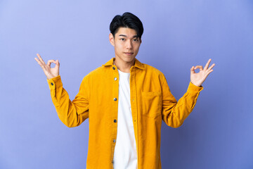 Young Chinese man isolated on purple background in zen pose