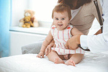 Fototapeta premium Happy girl-child at usual medical inspection. Doctor and female toddler patient in the clinic. Healthcare concept