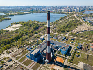 High chimney of a power plant on the outskirts of the city. Green spring steppe on the background. Aerial drone view.