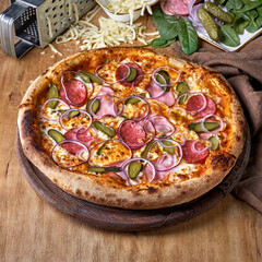 Pizza with carbonate, salami, gherkins and red onions on wooden background.