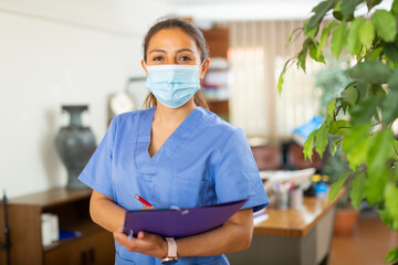 Fototapeta na wymiar Portrait of friendly female doctor in face mask standing in modern clinic