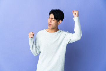 Fototapeta premium Young Chinese man isolated on purple background celebrating a victory