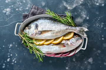 Raw dorado fresh fish or sea bream with ingredients for making lemon, thyme, garlic, cherry tomato and salt on a black slate, stone or concrete background. Top view with copy space.
