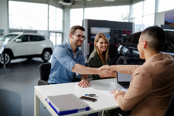 Male customer and female car dealer shaking hands at showroom. - obrazy, fototapety, plakaty