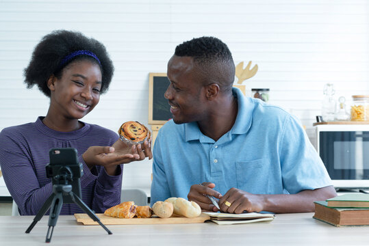 African girl blogger and father review their product and talking camera live recording video on social network at home, online merchants selling bakery on social media via mobile phones
