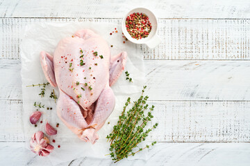 Whole raw chicken with ingredients for making pepper, lemon, thyme, garlic, cherry tomato, sorrel and salt in the kitchen on light grey slate, stone or concrete background. Top view with copy space