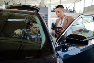 Test drive. Car buyer sitting in auto, choosing new automobile with seller In store.