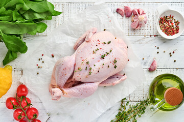 Whole raw chicken with ingredients for making pepper, lemon, thyme, garlic, cherry tomato, sorrel and salt in the kitchen on light grey slate, stone or concrete background. Top view with copy space