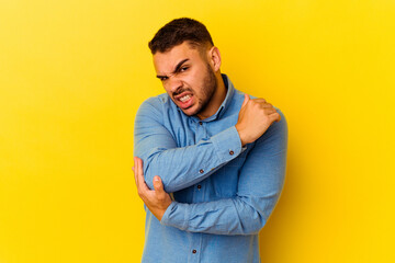 Young caucasian man isolated on yellow background massaging elbow, suffering after a bad movement.