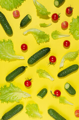 Juicy red tomato, green young cucumber, salad leaves with shadow on yellow background. Modern food pattern, top view, vertical.