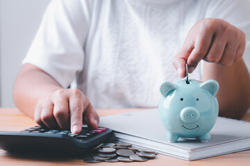 Obraz na płótnie Canvas Save money, Woman hand putting coins into blue piggy bank for account save money, Calculate saving money for future rate of return, retirement fund, business investment finance accounting concept.
