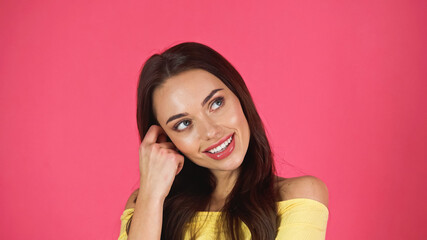 portrait of thoughtful young adult woman in yellow blouse with hand near face isolated on pink