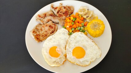Streak and fried eggs with vegetables on a white plate.