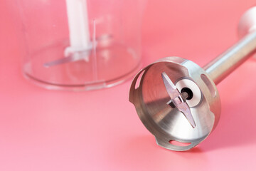 Steel hand blender and the bowl on pink background close-up.