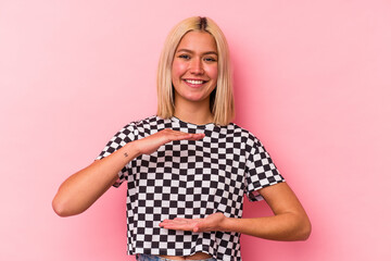 Young venezuelan woman isolated on pink background holding something with both hands, product presentation.