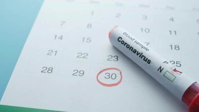 close up of corona virus blood test tube and calendar on table 