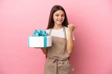 Little girl with a big cake over isolated pink background pointing to the side to present a product