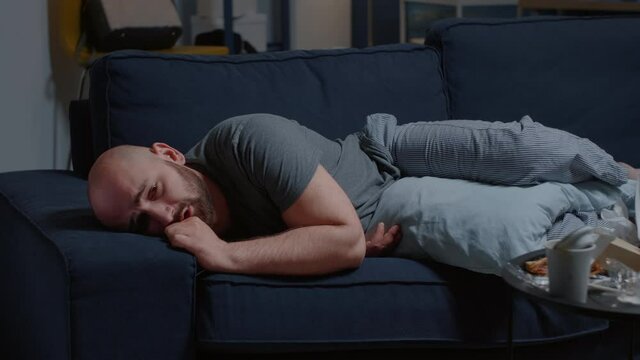 Depressed disappointed man with broken heart because of break up crying abundantly laying on sofa having psychotic moment. Male trying to stifle pain and frustration, psychological suicidal thoughts