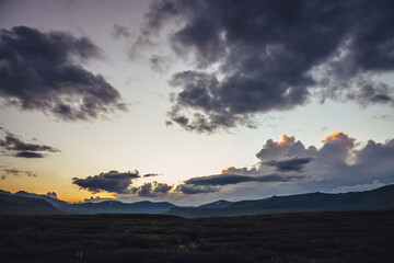 Beautiful mountain scenery with golden dawn light in cloudy sky. Scenic mountain landscape with illuminating color in sunset sky. Silhouettes of mountains on sunrise. Gold illuminating sunlight in sky