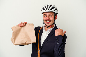 Young business caucasian man wearing bike helmet and holding take way food isolated on white background points with thumb finger away, laughing and carefree.