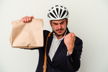 Young business caucasian man wearing bike helmet and holding take way food isolated on white background showing fist to camera, aggressive facial expression.