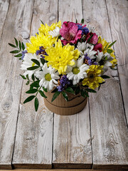 Gift bouquet of flowers to a round cardboard hat box. White and yellow chrysanthemums in a gift box on a wooden background. A handmade present for a birthday, Valentines Day or a wedding. Copy space