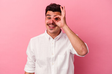 Young caucasian man isolated on pink background excited keeping ok gesture on eye.