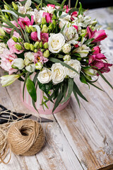 Gift bouquets of flowers to a cardboard box, packing twine and scissors. Pink rose and alstrameria in a round gift box on a wooden background. Vertical shot. Copy space.