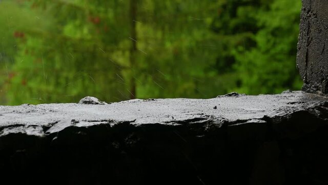 Close up view of the rain in nature. Focus on droplets falling on concrete window. Gloomy and rainy day in mountains. Shallow depth of field, static shot, real time