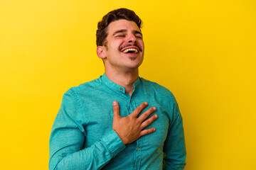 Young caucasian man isolated on yellow background laughs out loudly keeping hand on chest.