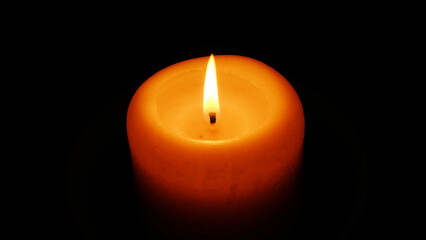 Top of an orange candle glowing in the dark, with the flame being still and straight.