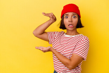 Young mixed race woman isolated on yellow background shocked and amazed holding a copy space between hands.