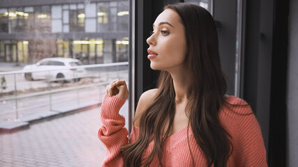 tense young adult woman standing near window in modern loft