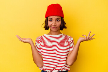 Young mixed race woman isolated on yellow background doubting and shrugging shoulders in...