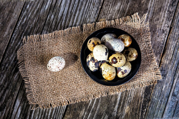 Quail eggs in a plate on a wooden background, top view