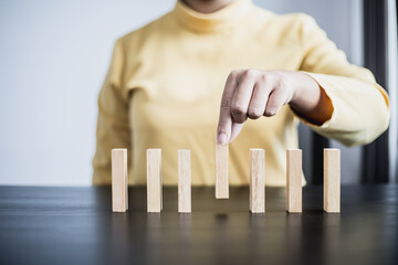 Businesswoman picking up a block of wood from a row, solving problems that arise during planned...