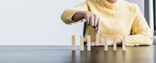 Businesswoman picking up a block of wood from a row, solving problems that arise during planned...