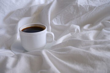 Cup of coffee on white bed linen.