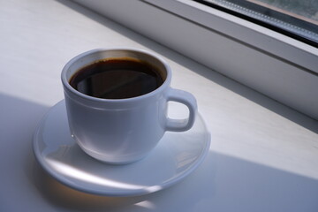 A cup of coffee on the windowsill. The sun's rays on the windowsill.