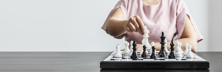 Businesswoman holding white chess pieces on a chessboard, comparing chessboard to business administration, planning operations to achieve goals and problem-solving. Business administration concept.