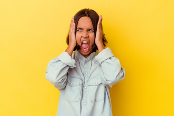 Young mixed race woman isolated on yellow background covering ears with hands trying not to hear too loud sound.